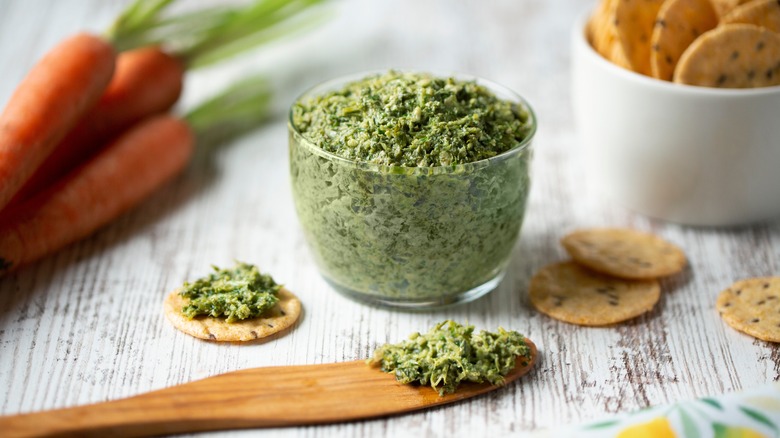 Bowl of carrot top pesto with crackers and wooden spoon