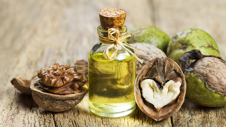 A stoppered glass bottle of green oil with whole and cracked walnuts on a table