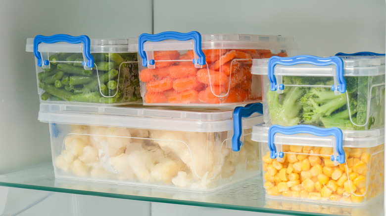 Clear storage bins on fridge shelf containing beans, carrots, broccoli, corn, and cauliflower