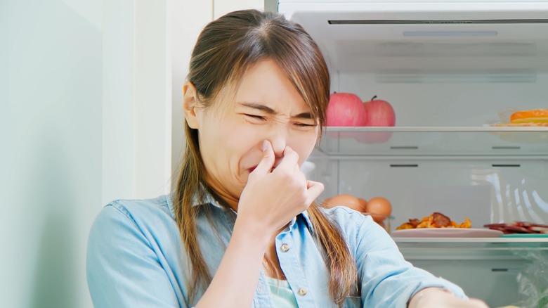woman smelling something bad from fridge