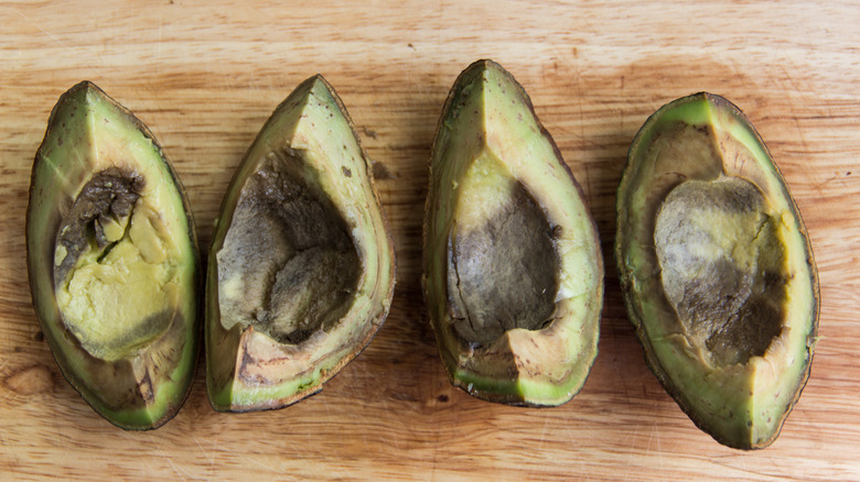 Four pieces of rotten avocado on a wooden board