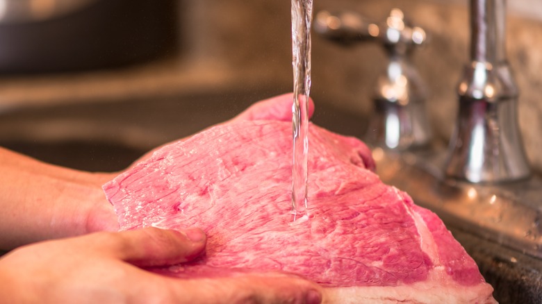 Person washing meat in sink