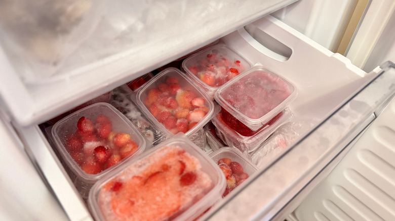 Plastic containers of strawberries in a freezer drawer