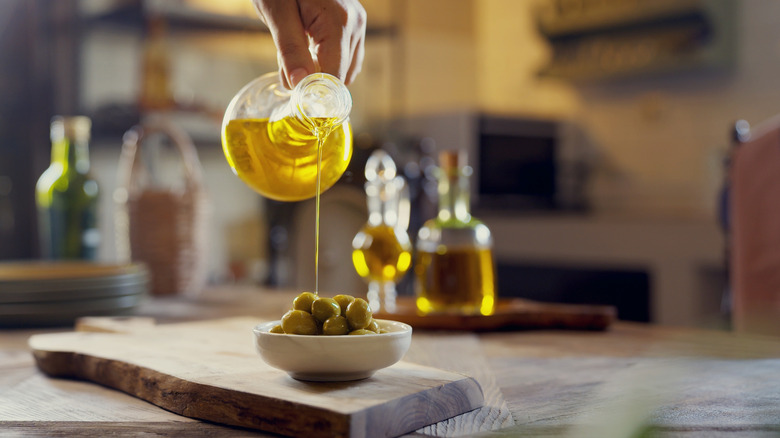 person pouring olive oil onto whole olives