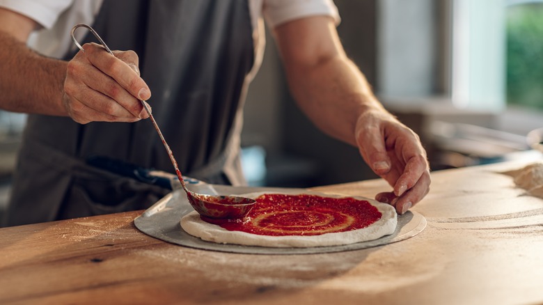 Ladling sauce over pizza dough