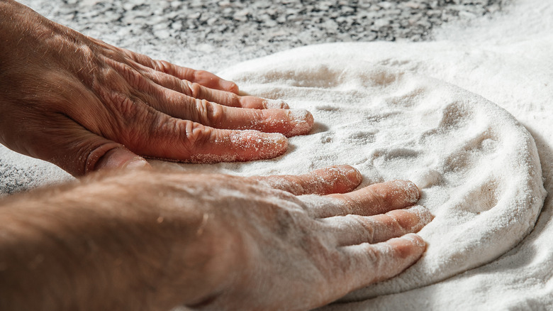 hands stretching pizza dough on a marble surface