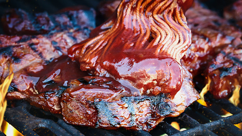 brushing barbecue sauce on meat on the grill