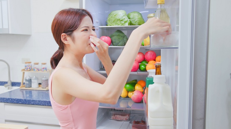 Woman holding nose by refrigerator