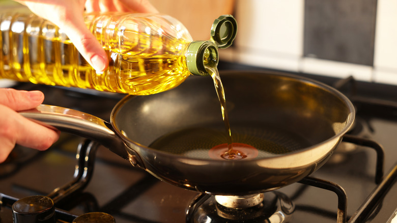 Home cook pouring vegetable oil into a hot frying pan