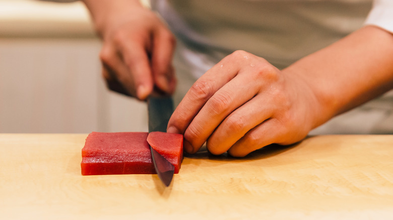 Chef with sushi knife slicing tuna