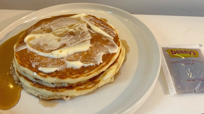 Stack of Denny's pancakes with butter and syrup on white plate