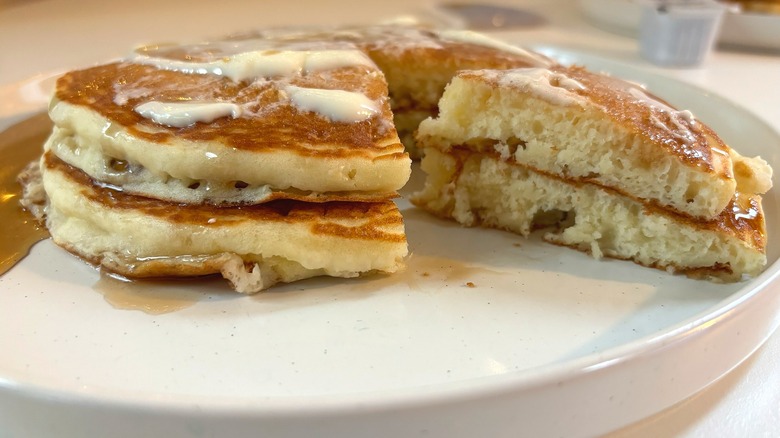 Stack of Denny's pancakes sliced on white plate with butter and syrup