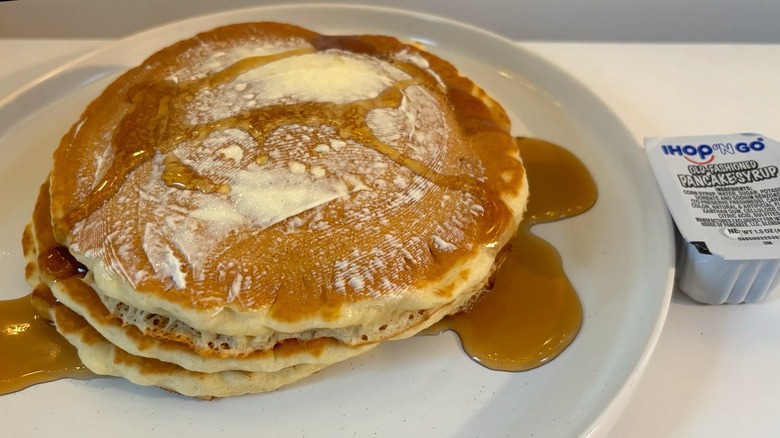 Stack of IHOP pancakes on white plate with butter and maple syrup