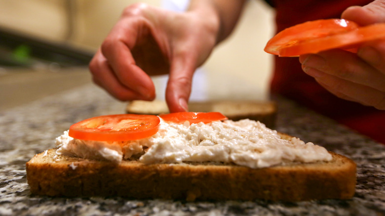 Person placing tomatoes on sandwich