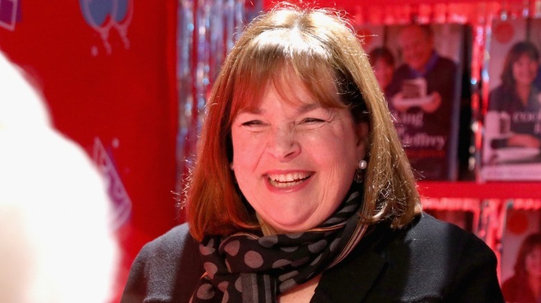 Ina Garten smiling at a book signing with a red background