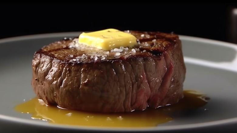 A cooked filet mignon with a knob of butter on top on a plate