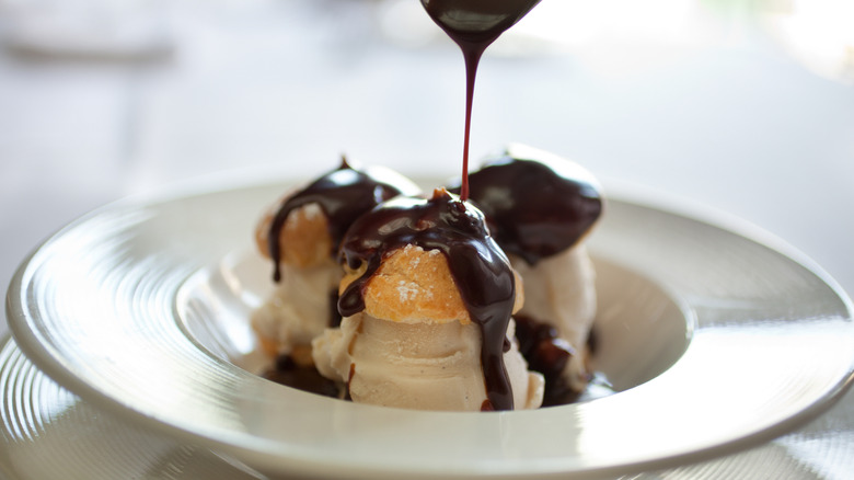 Chocolate pouring onto profiteroles on plate