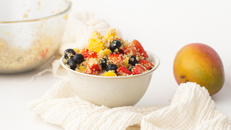 quinoa sprinkled fruit salad with whole mango and glass bowl in the background