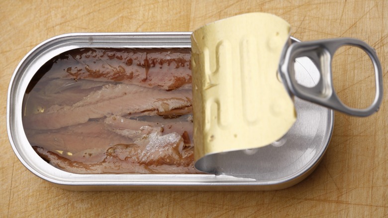 Top-down view of an open tin of anchovies in oil