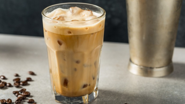 A glass of shaken espresso next to coffee beans