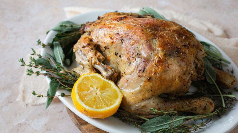 whole chicken on platter with herbs, lemon