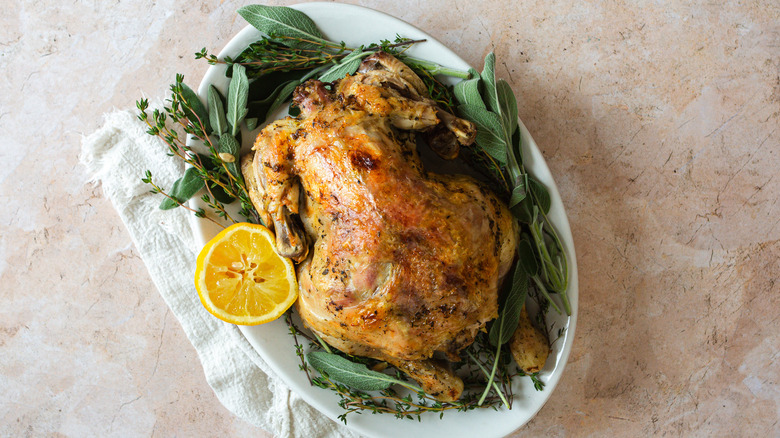 whole chicken on platter with herbs, lemon