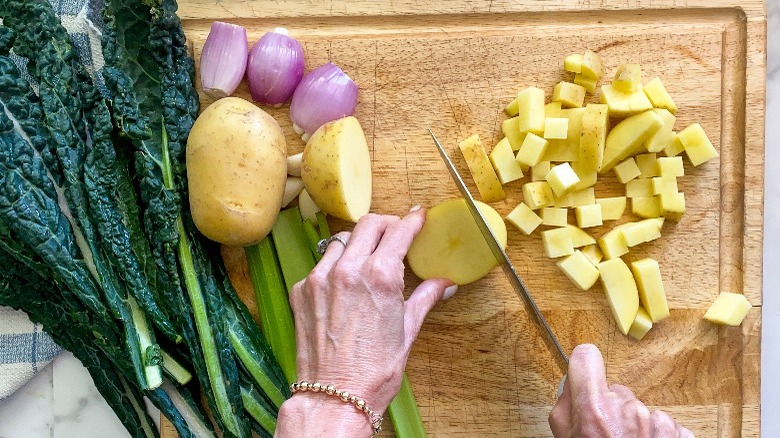 cutting potato on board with other vegetables