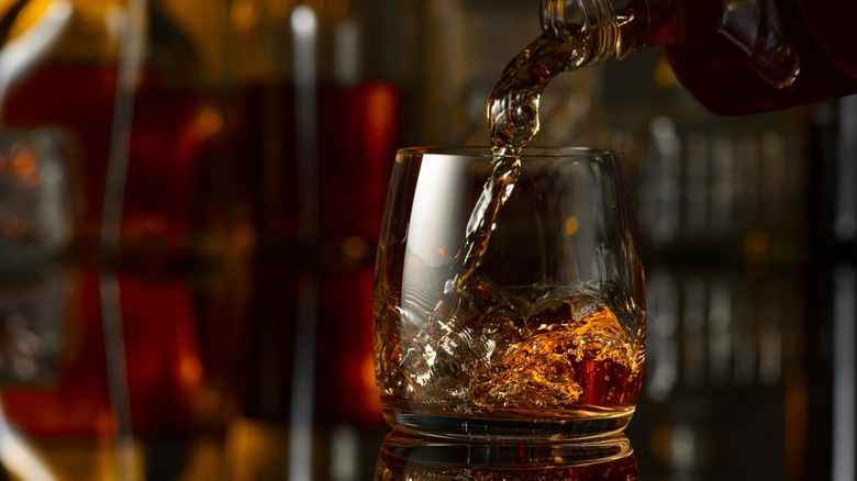 Whiskey being poured into a glass over ice