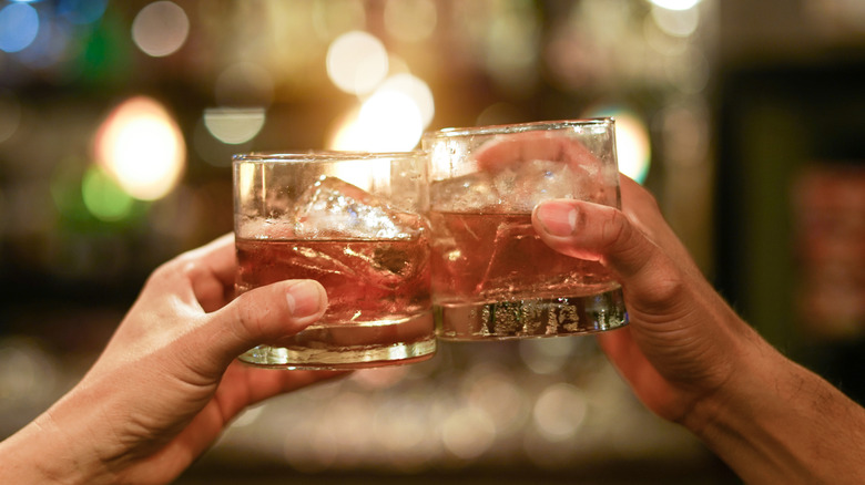 Two hands clinking glasses of bourbon on the rocks