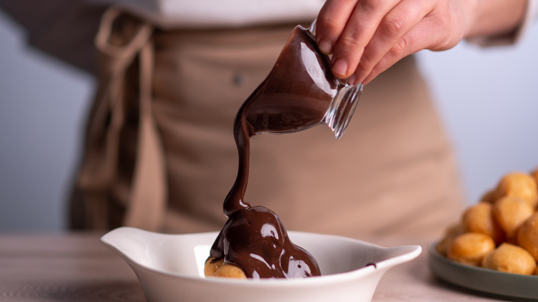 Person pouring chocolate sauce from jug over dessert