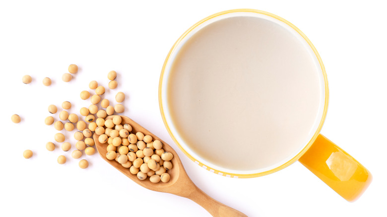 soy milk in a yellow cup next to soybeans