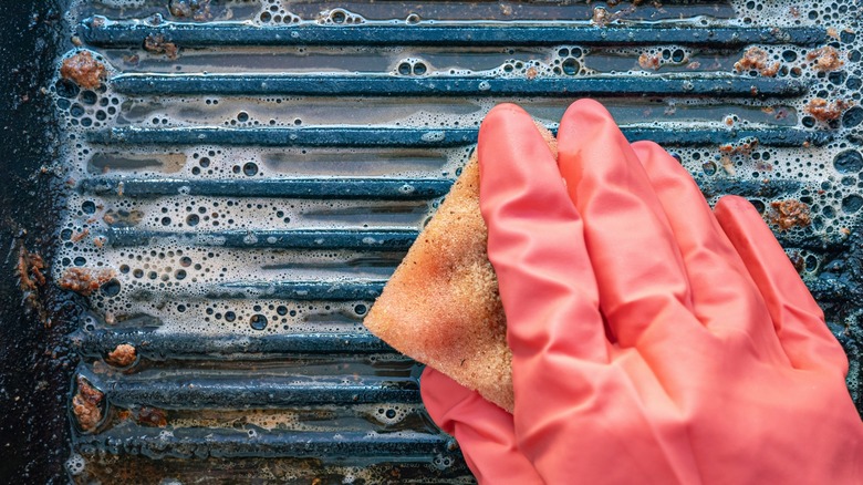 Pink-gloved hand cleaning a grill with a sponge