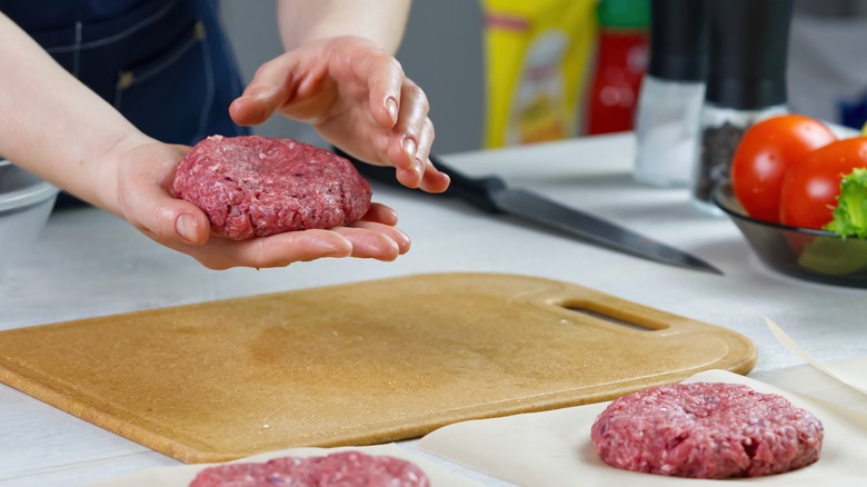 Person prepping several beef patties.