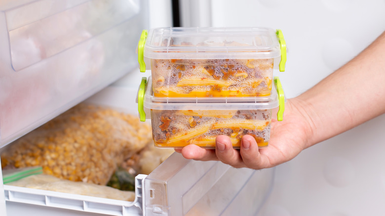 Hand holding frozen containers near fridge