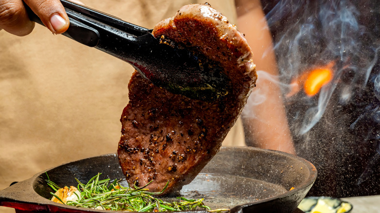 Picanha steak picked up by tongs from a pan