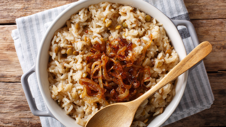 Top-down view of rice and lentils in a pot with a wooden spoon on a wood table