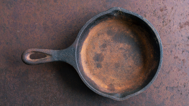 A rusty cast iron skillet sits on a metal table