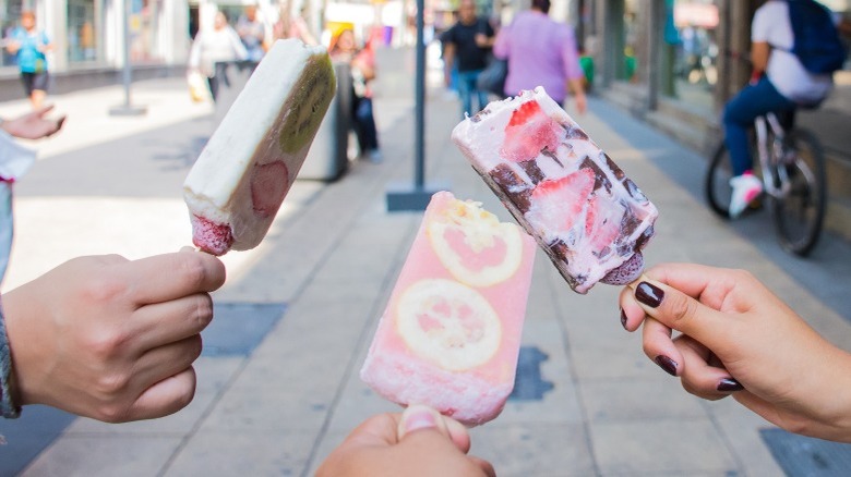 Hands holding three fruit paletas outside