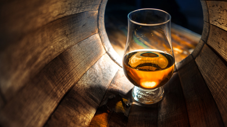 Glass of bourbon in oak barrel 