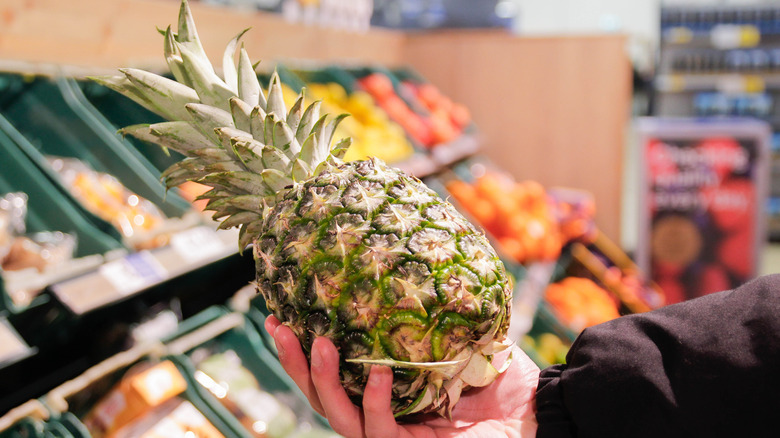 Hand holding pineapple in supermarket aisle