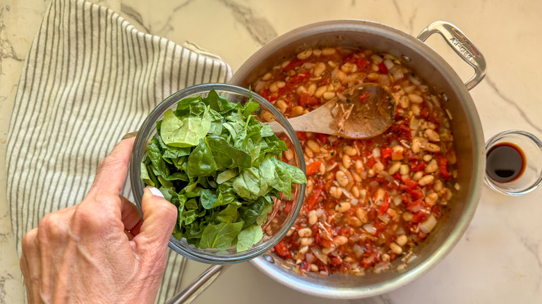 hand adding spinach to skillet