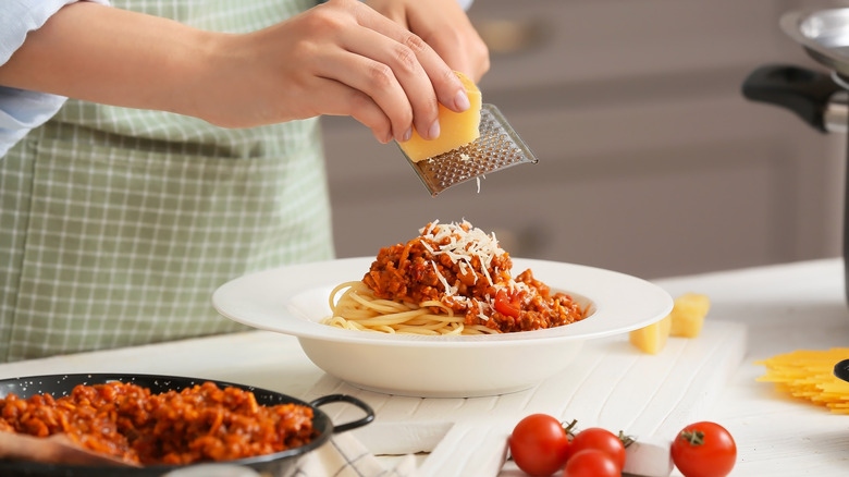 hands grating cheese over pasta