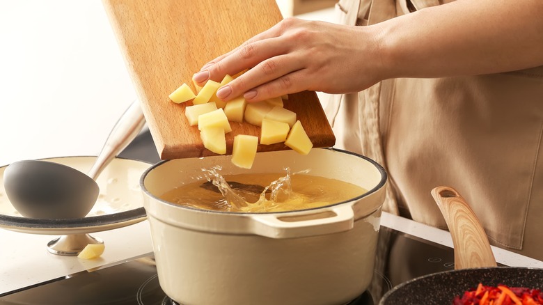 adding potatoes to a soup cooking