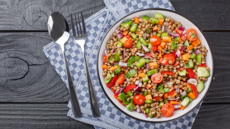 bowl of lentils, tomatoes, cucumbers with fork and spoon