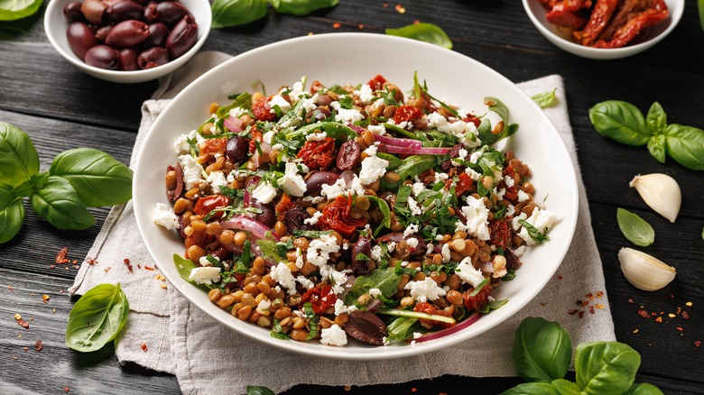 arugula salad with lentils, olives, feta cheese in white bowl