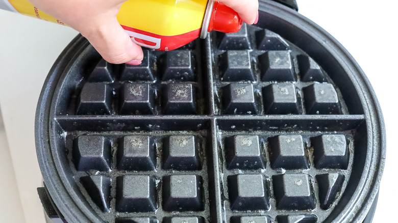 waffle iron being greased with cooking spray