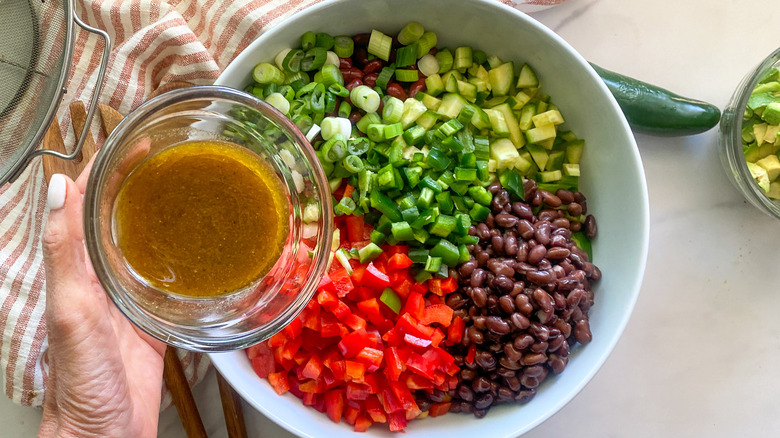 hand pouring dressing into salad