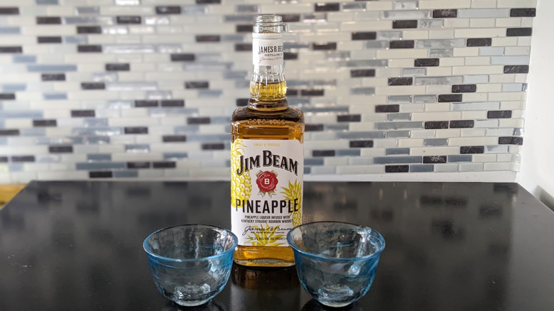 Jim Beam Pineapple bottle and glasses against backsplash