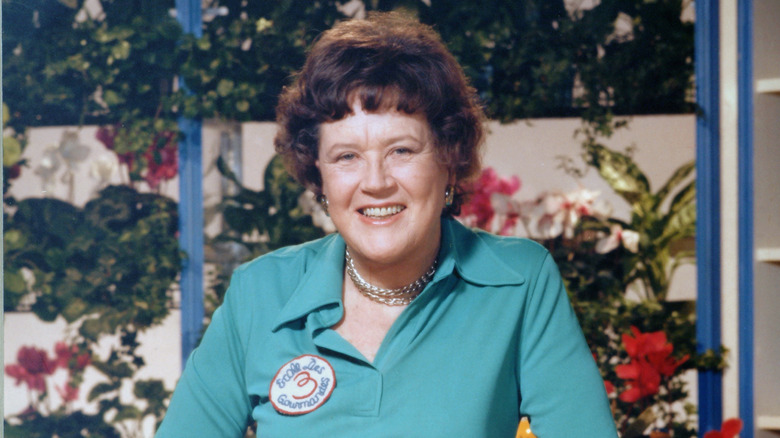 Julia Child smiling in front of a background of plants and greenery