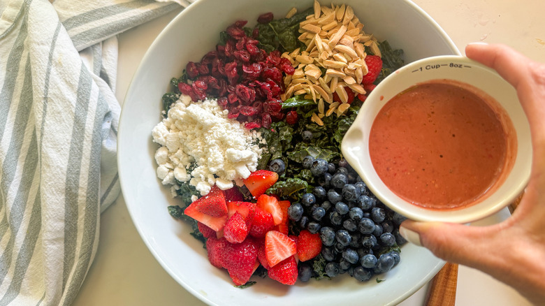 hand adding dressing to salad